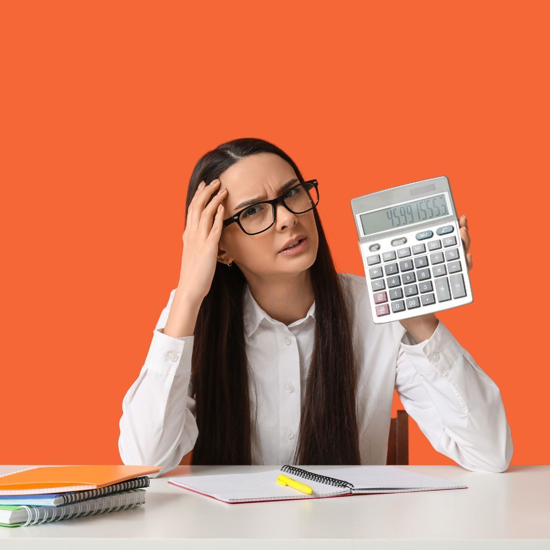 Woman at desk looking confused, holding a calculator against an orange background.