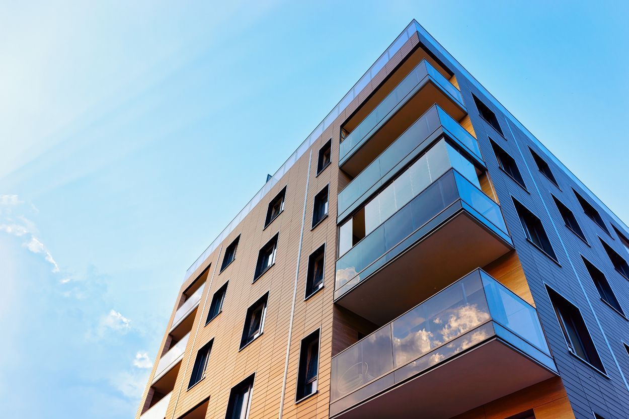 Vue du bas d'un immeuble de plusieurs étages avec le ciel bleu en arrière plan.