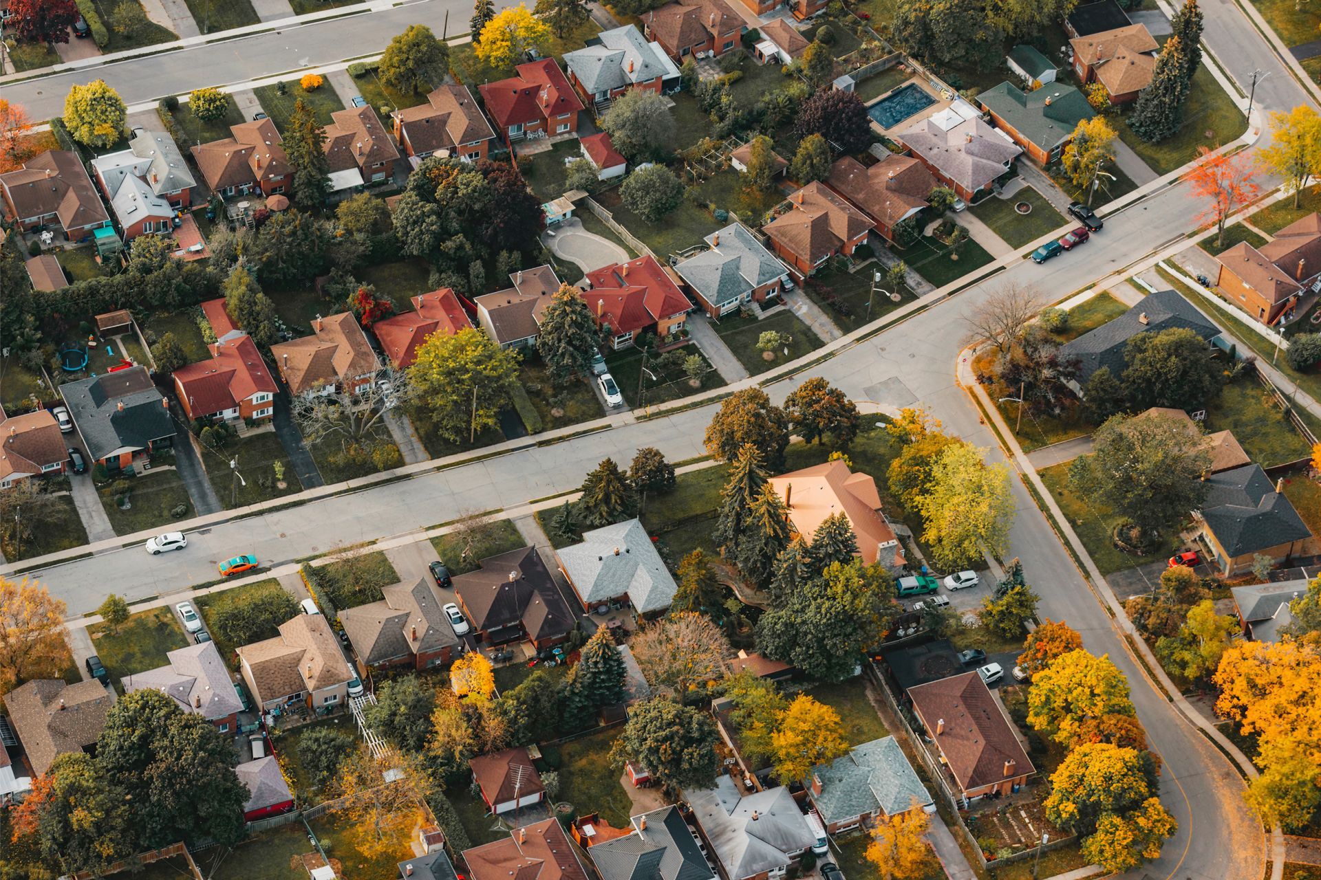 Aerial view of a residential neighborhood with detached houses, tree-lined streets, and autumn foliage.