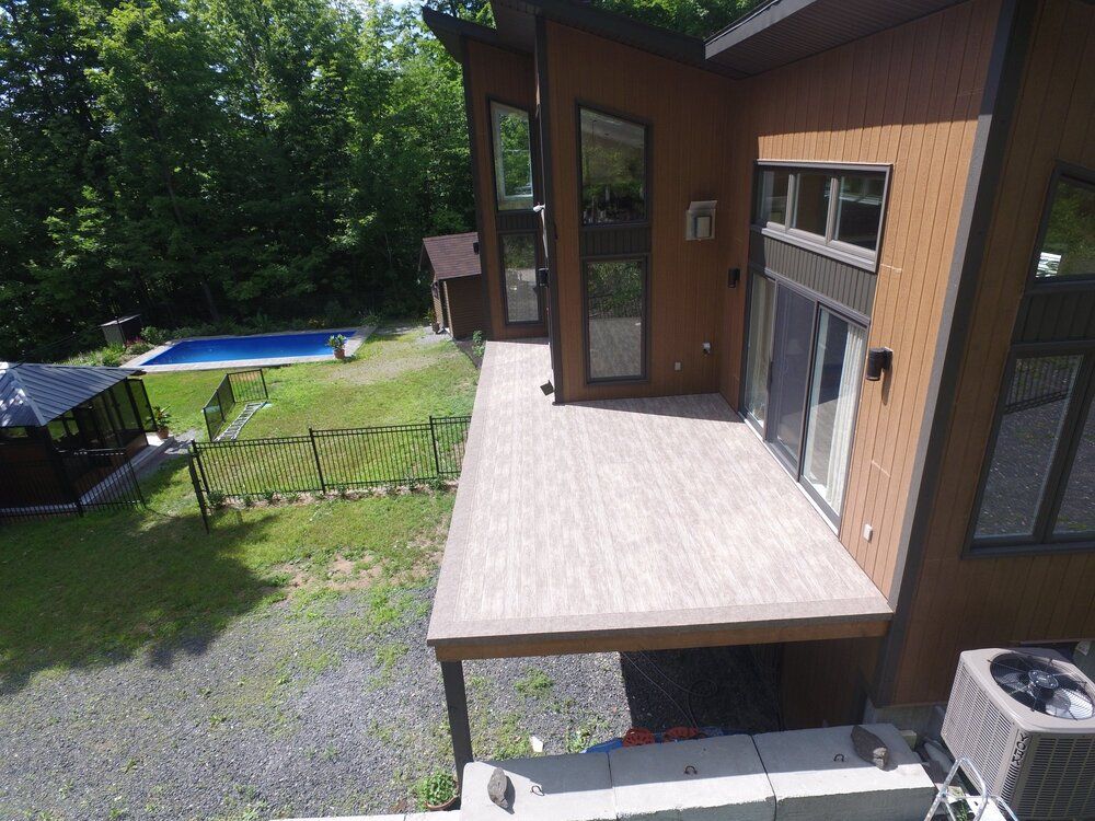 Une vue aérienne d'une maison avec une grande terrasse en membrane de pvc et une piscine dans l'arrière-cour.
