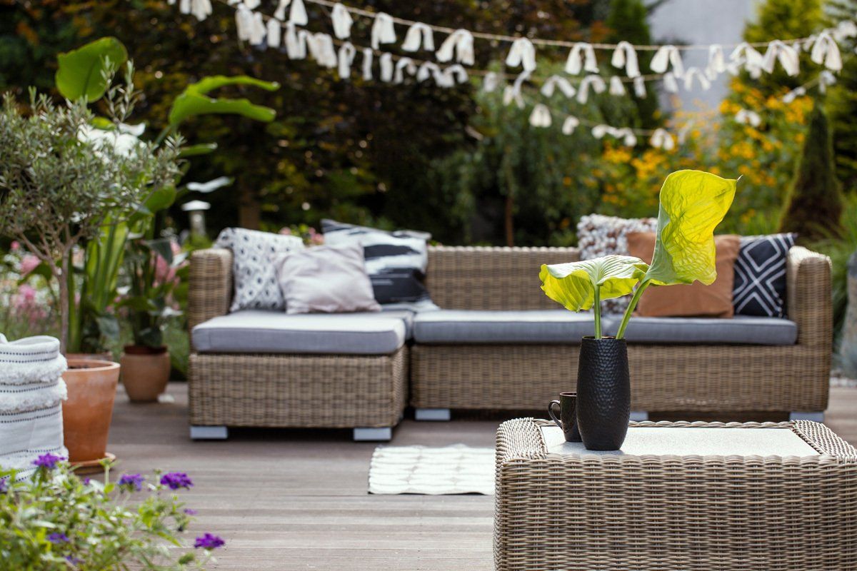 Un canapé en osier est assis sur une terrasse en bois à côté d'une table basse.