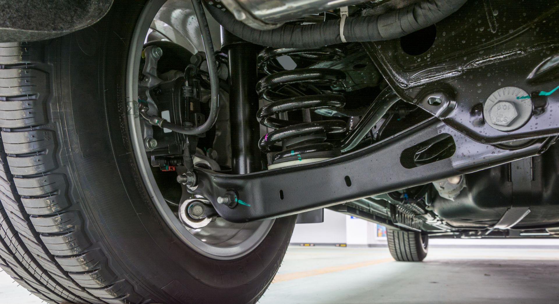 Undercarriage of a vehicle showing a black suspension arm, tire, and coil spring.