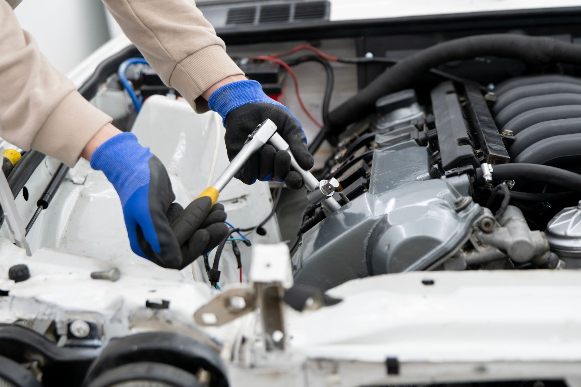 Hands wearing blue gloves working on a car engine with tools.