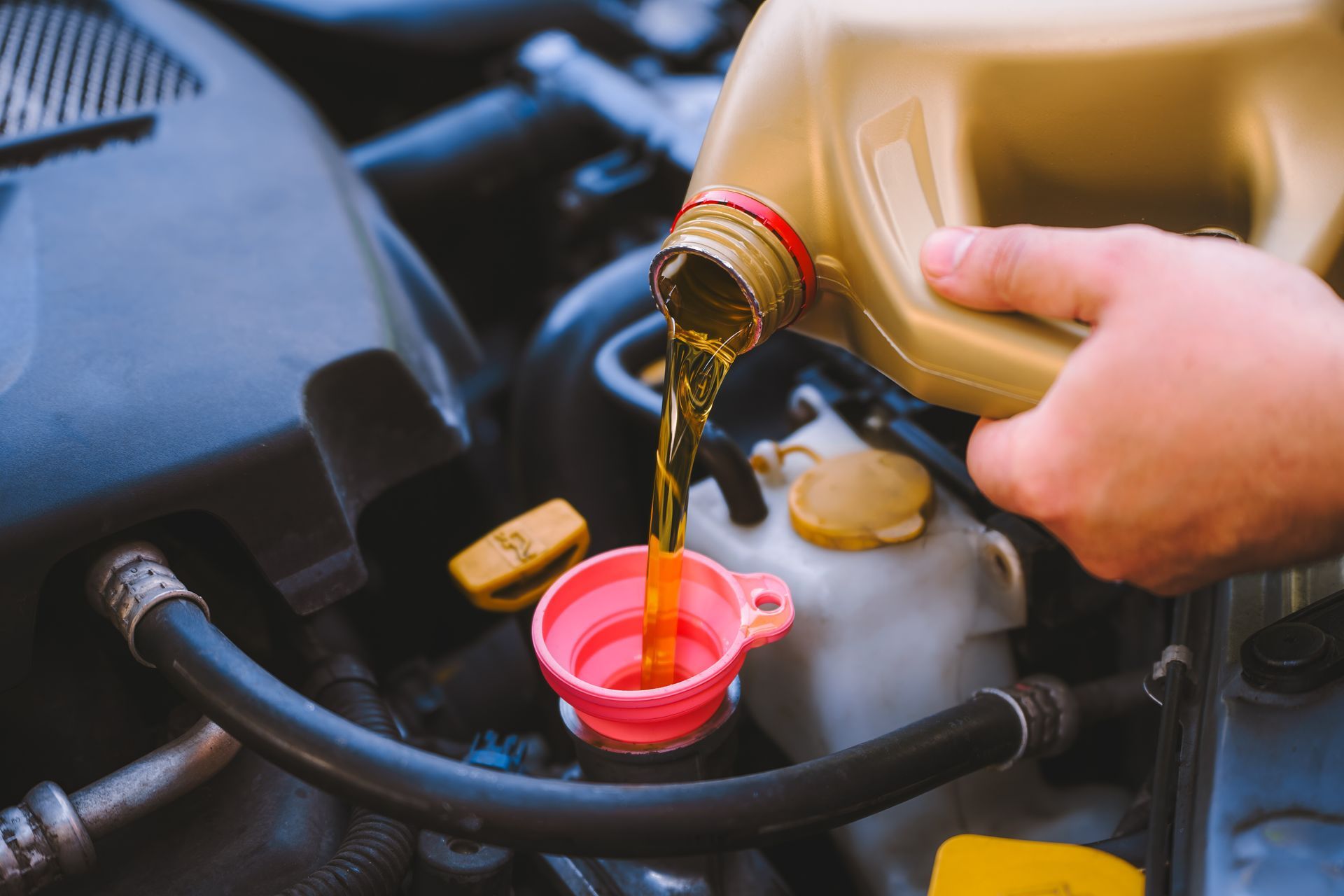 Pouring motor oil into a car's engine. Yellow oil flowing from a container into a pink funnel.