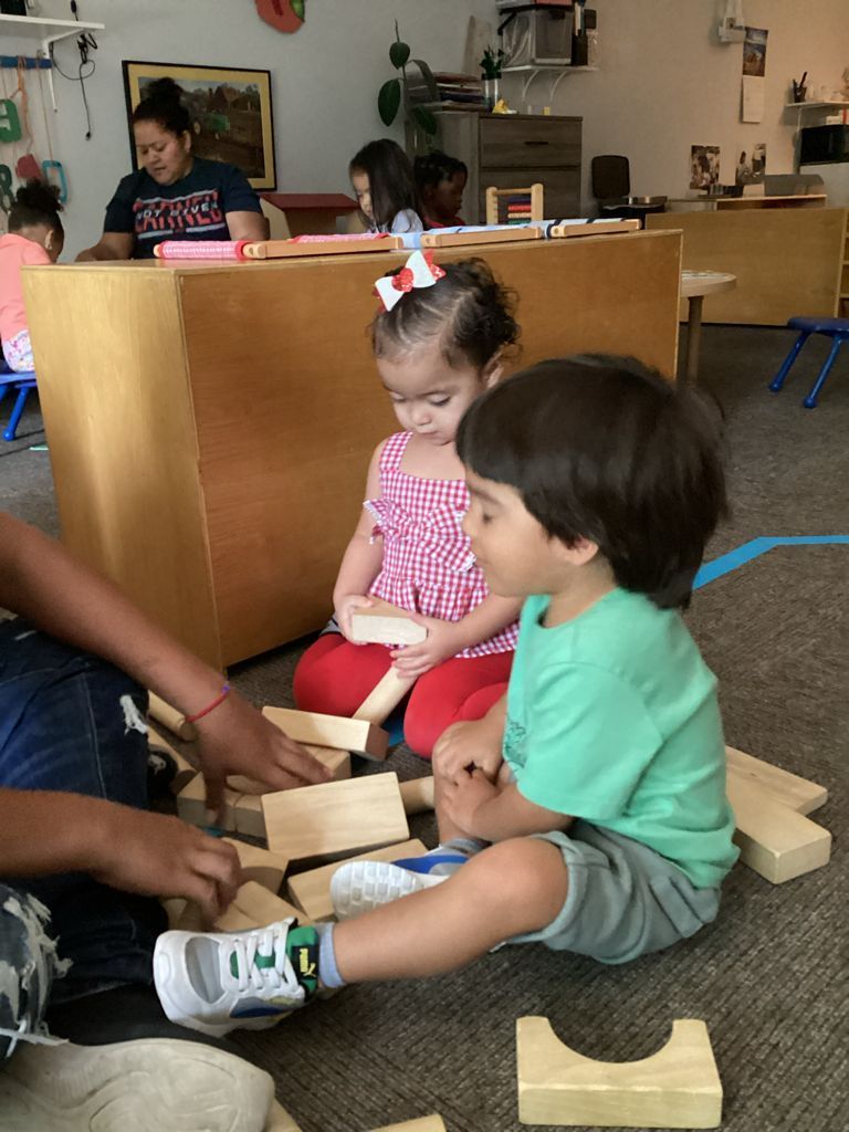 A boy and a girl are sitting on the floor playing with wooden blocks.