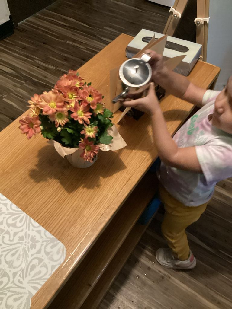 A little girl is playing with a teapot on a wooden table.