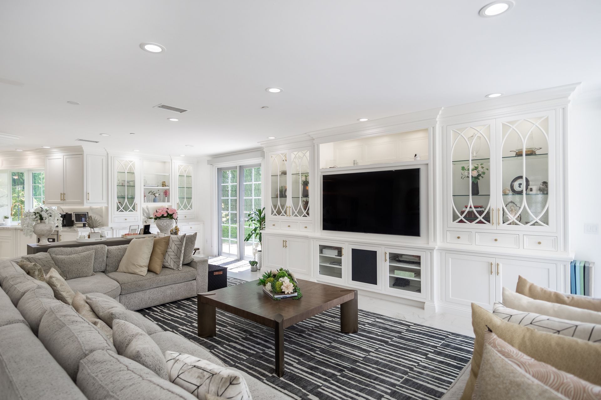 Bright white living room with gray sofas, a dark coffee table, built-in cabinets, and a wall-mounted TV.