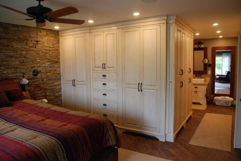 Spacious bedroom with a bed, white built-in wardrobe, brick accent wall, and ceiling fan