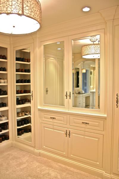 Built-in cream closet with glass shelves, drawers, and mirrored doors in a carpeted dressing room
