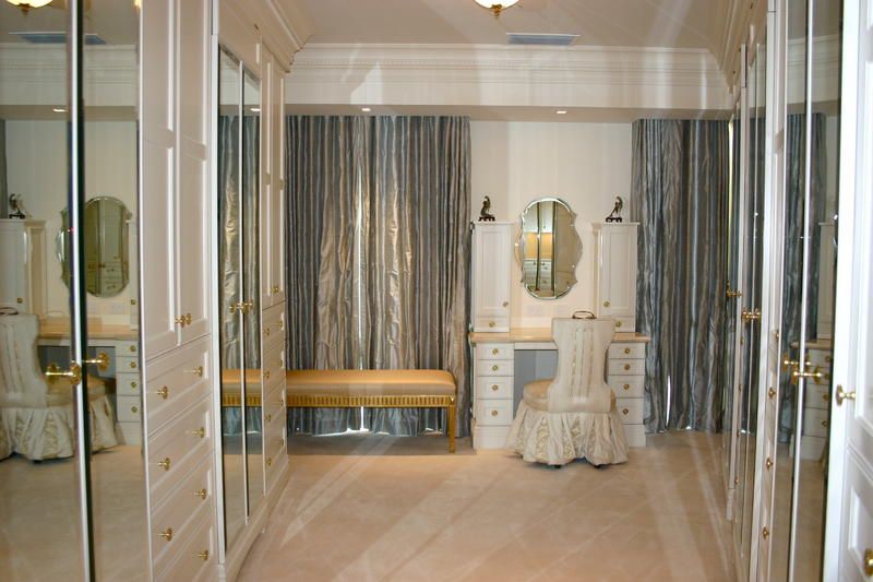 Bright dressing room with mirrored closet doors, wooden bench, and ornate white vanity under striped curtains