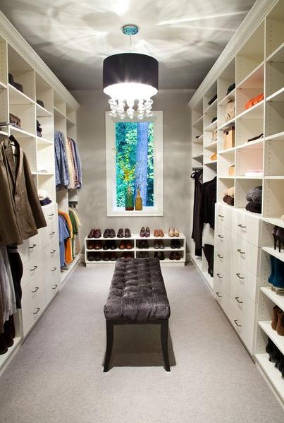 Bright walk-in closet with built-in shelves, hanging clothes, a bench, and a window at the end.