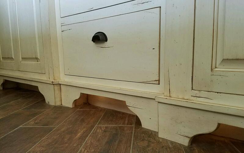 Cream-colored cabinet base with decorative cutouts and a black knob over a tiled floor.
