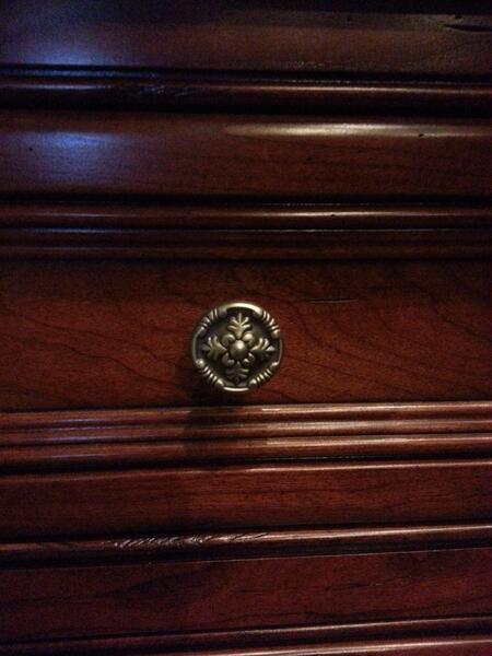 Close-up of a polished wooden dresser drawer with a round floral brass knob.