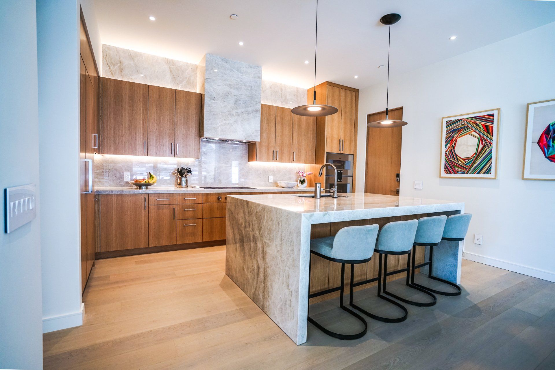 Modern kitchen with wood cabinets, marble island, and three blue bar stools
