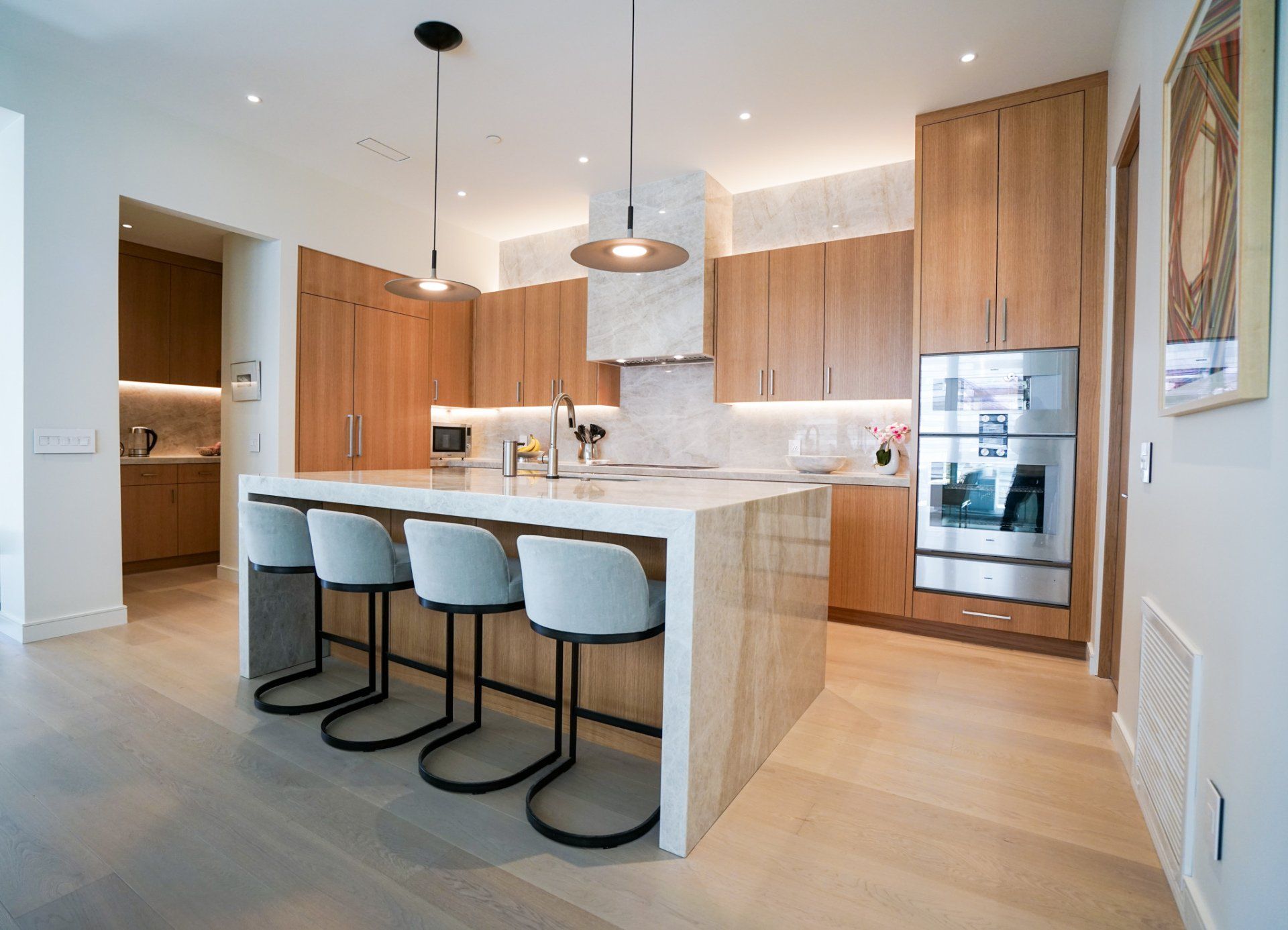 Modern kitchen with light wood cabinets, marble island, and four blue bar stools
