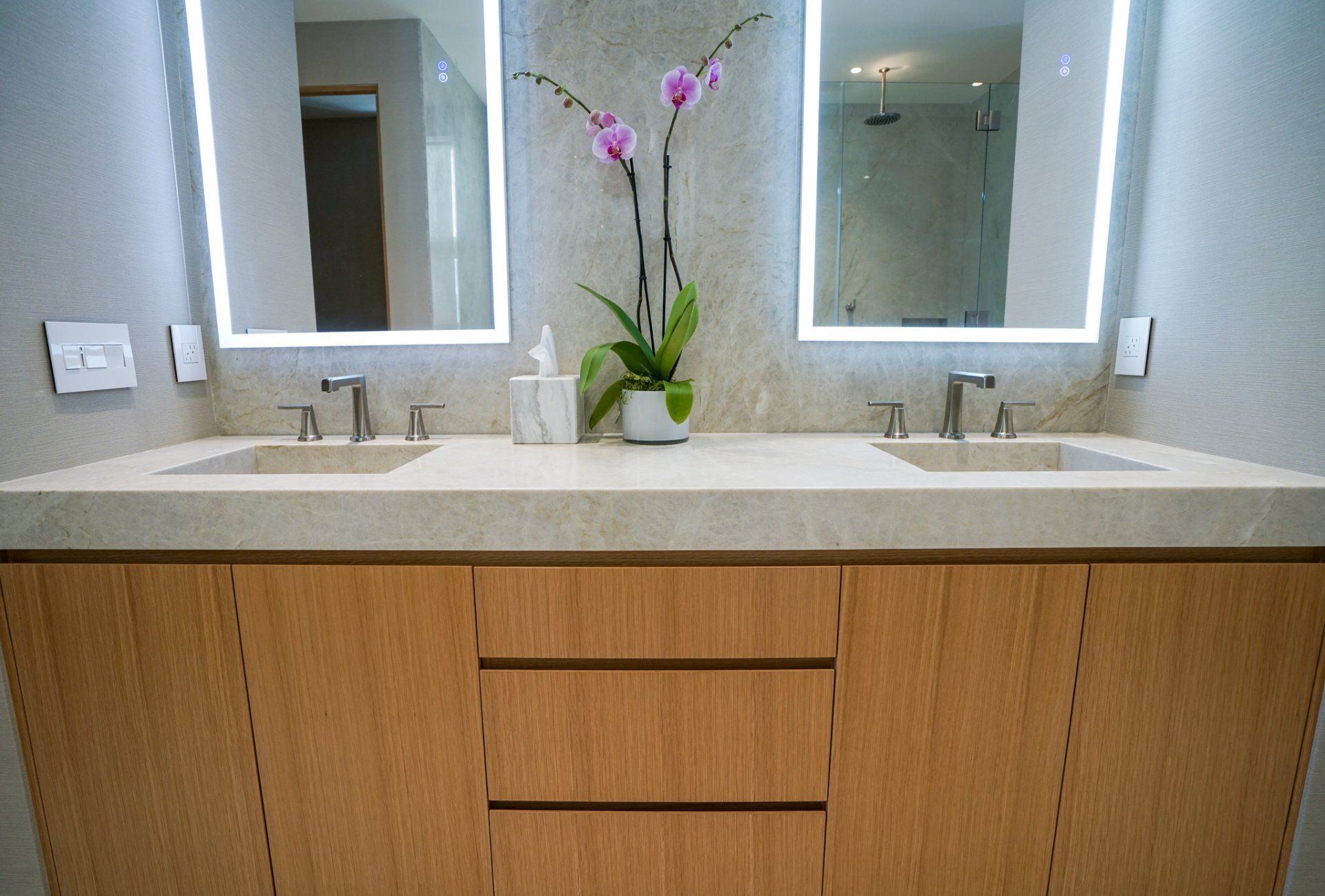 Modern bathroom vanity with double sinks, mirrors, and a vase of pink orchids on the counter