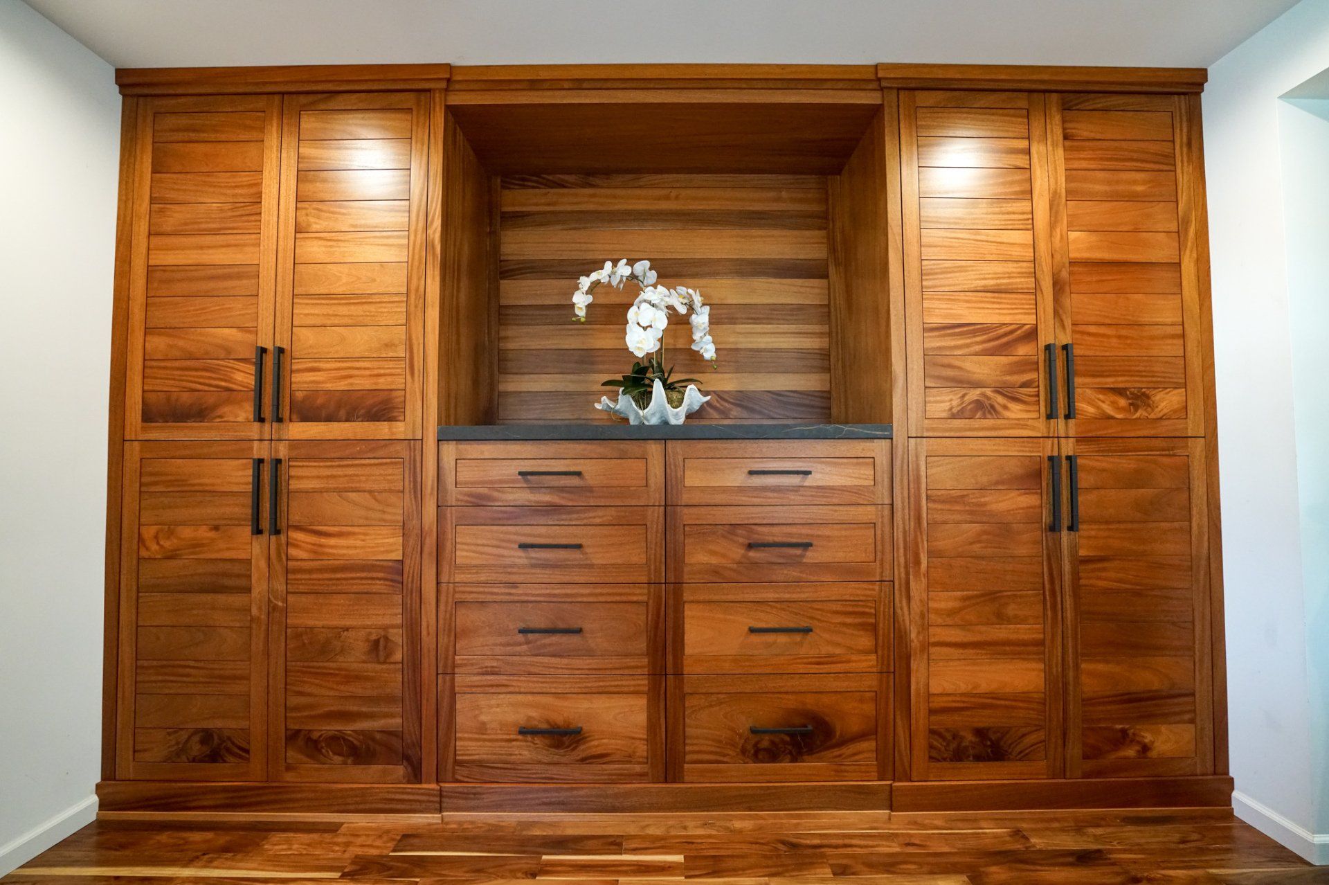 Built-in wooden wall unit with cabinets, drawers, and a floral centerpiece in a formal room