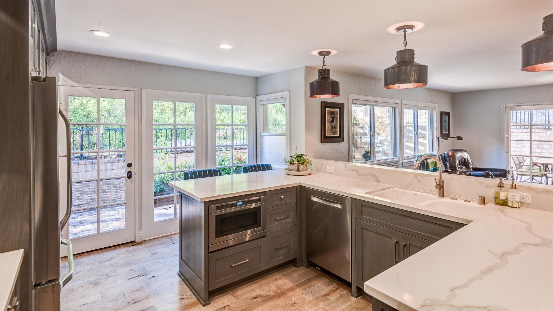 Bright modern kitchen with white cabinets, gray island, pendant lights, and French doors to a patio