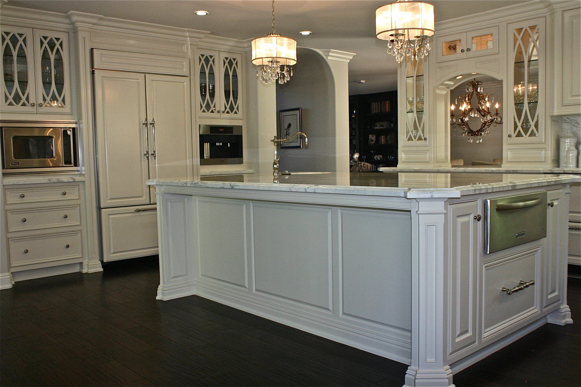 Elegant white kitchen with a large island, chandeliers, and decorative cabinets