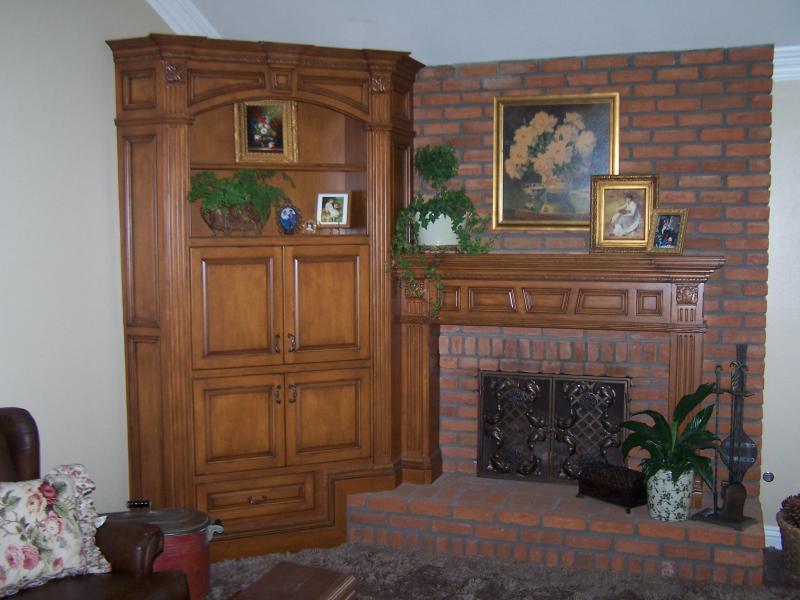 Living room corner with a brick fireplace, wooden cabinet, framed art, and potted plants