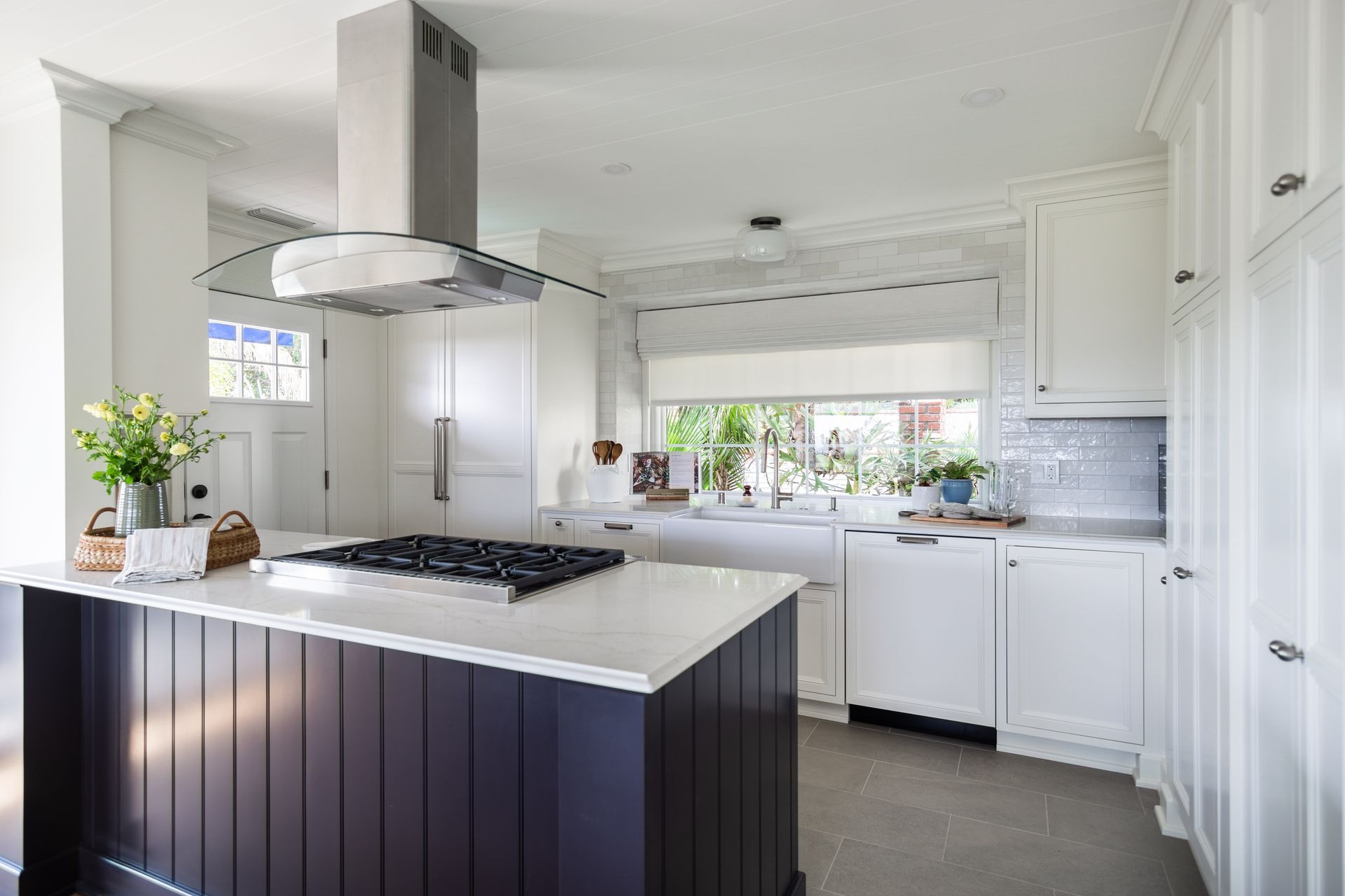 Bright white kitchen with a dark island, gas range, and large window over the sink
