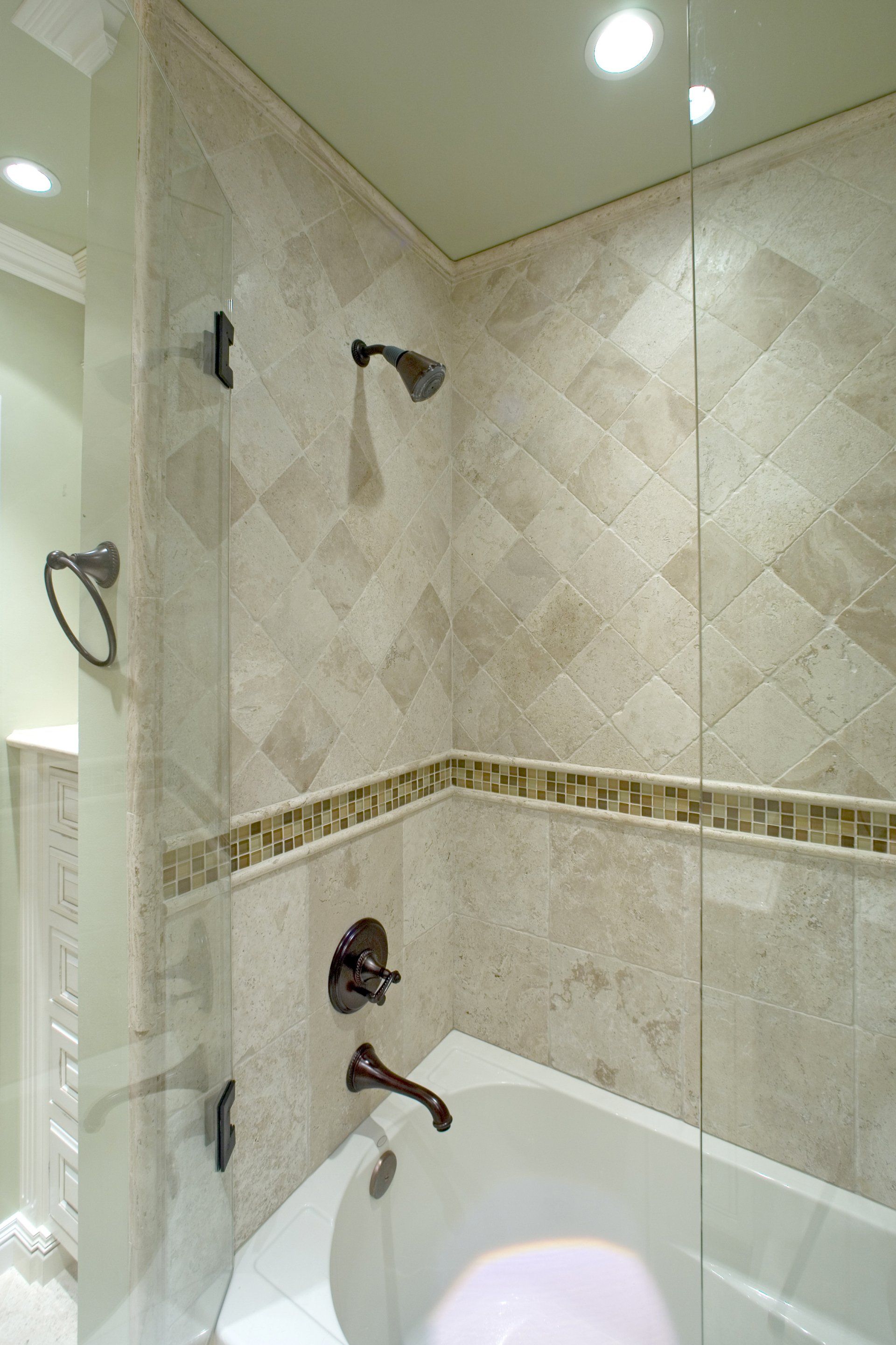 Bathroom with beige tiled shower, glass partition, and white bathtub under ceiling lights