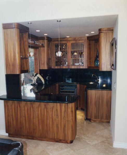 Dark wood kitchen with black countertops, tiled floor, and recessed lighting, viewed from the doorway