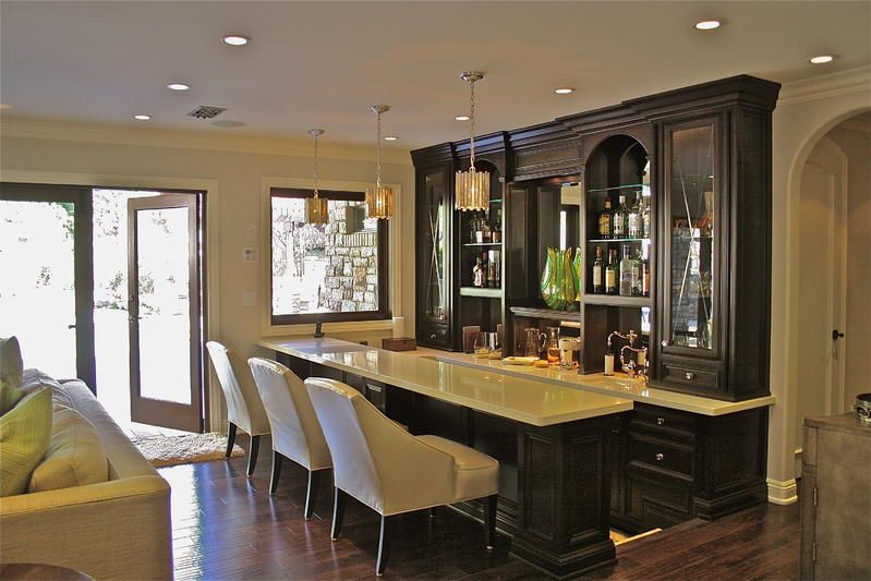 Modern home bar with dark cabinetry, marble island, and stools in a warmly lit open-plan room