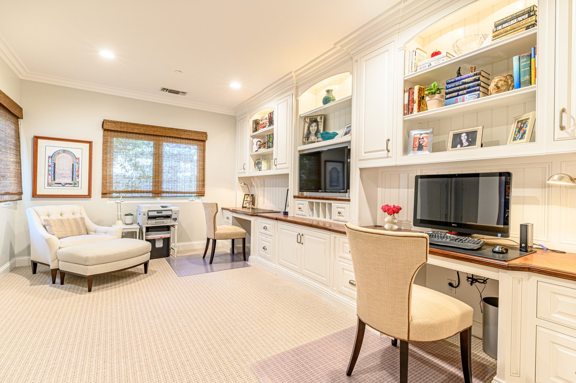 Bright home office with built-in shelves, desk, computer, and a cozy seating area by the window.