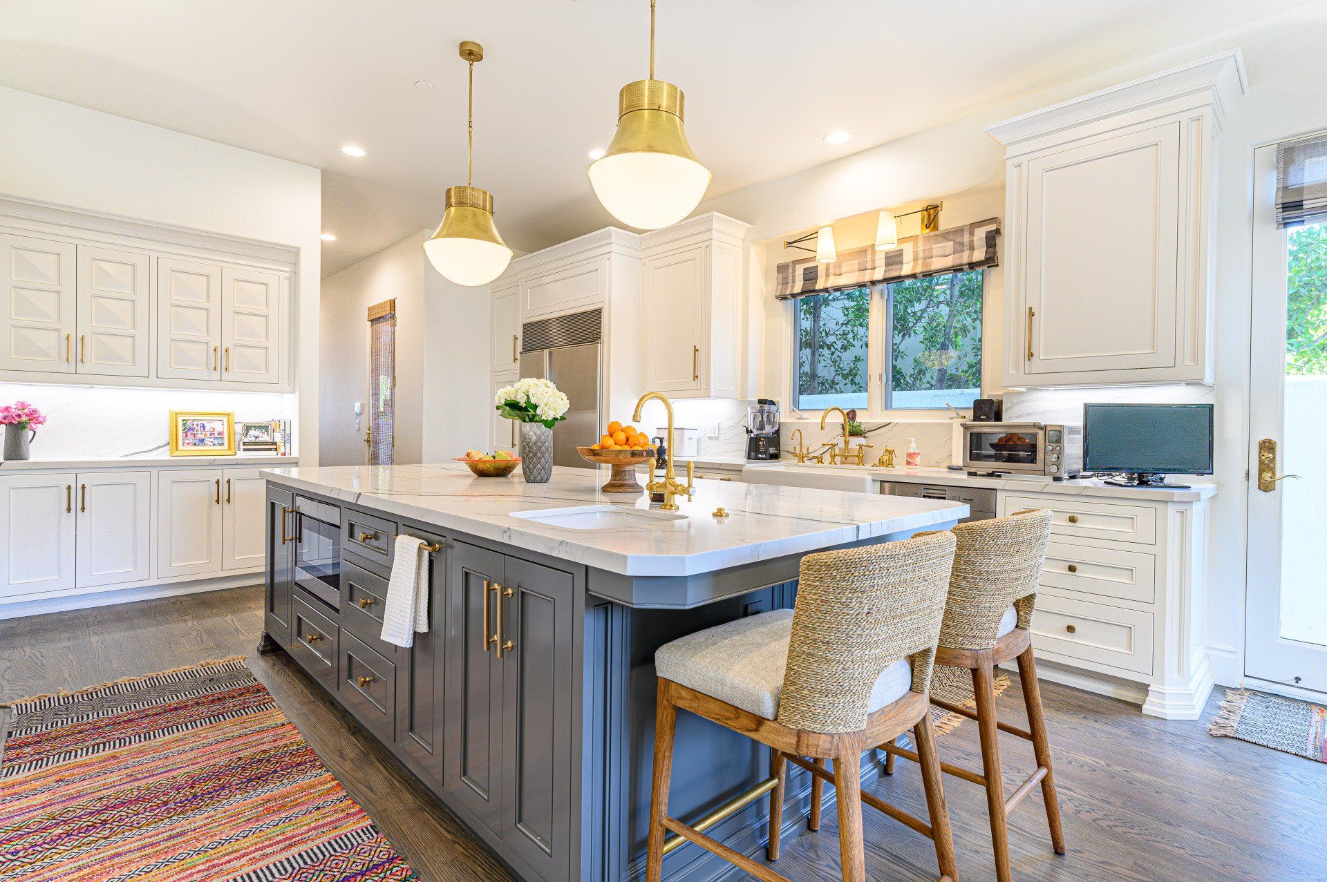 Bright white kitchen with a large dark island, pendant lights, barstools, and patterned rug