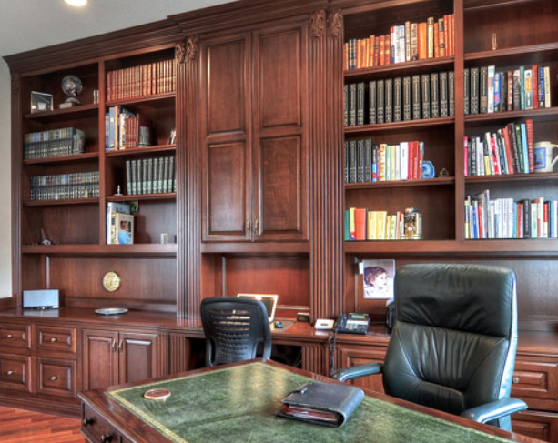 Wood-paneled office with bookshelves, desk, and black leather chairs