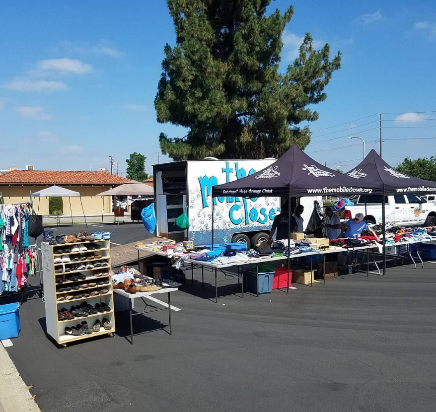 Outdoor flea market with tables of clothes and shoes under black tents on a sunny street