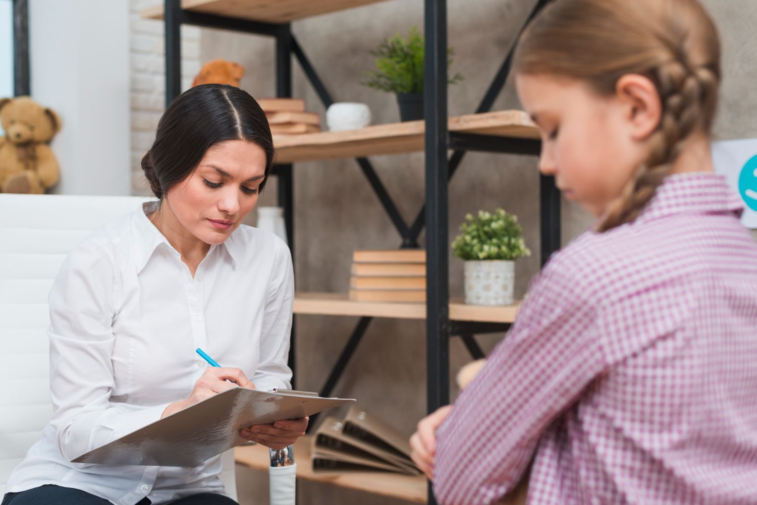 A woman is talking to a young girl while holding a clipboard during an ABA therapy session in North Carolina