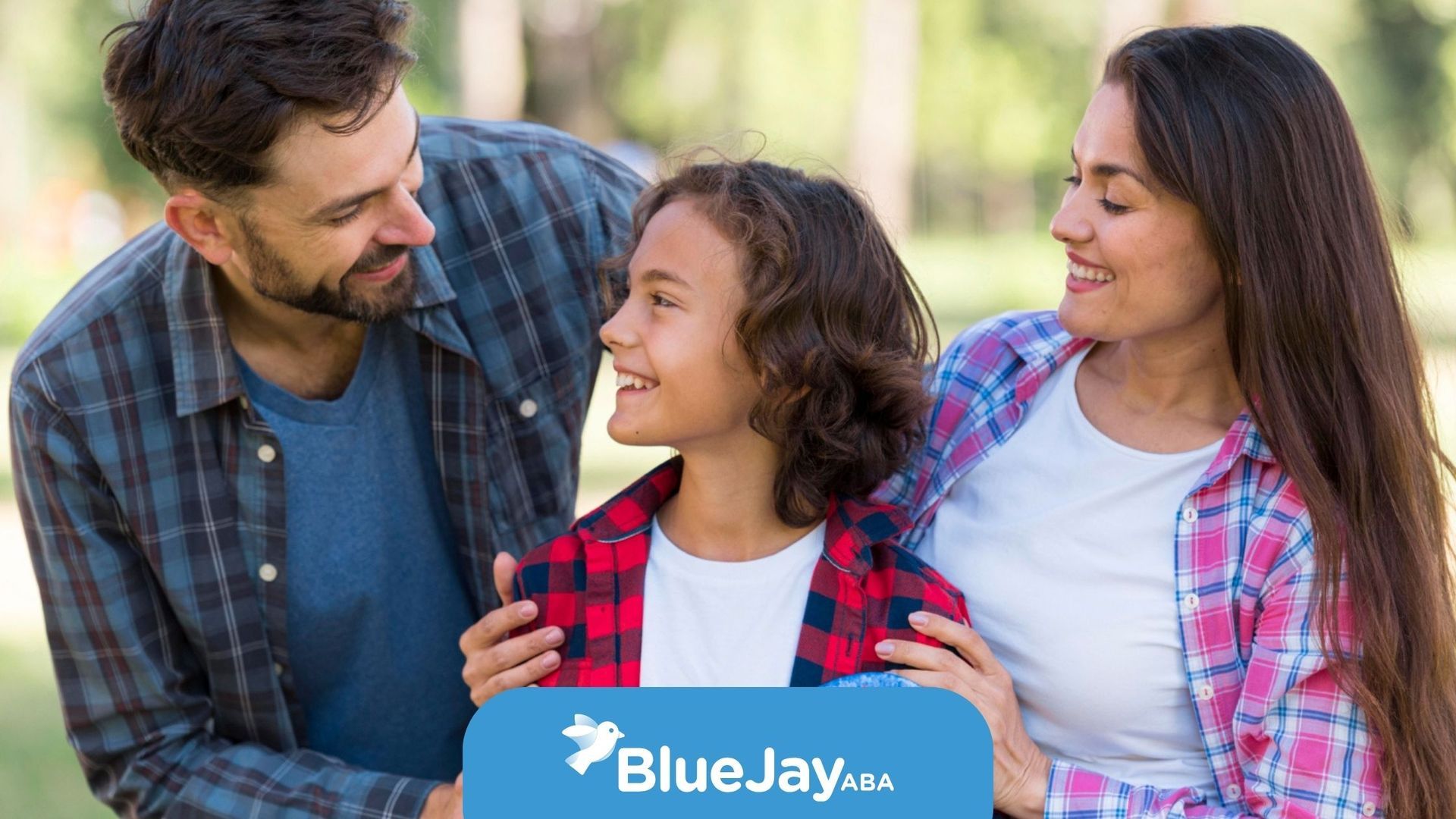 Three people chatting and smiling outdoors, with one person’s arm around a child in a plaid shirt.