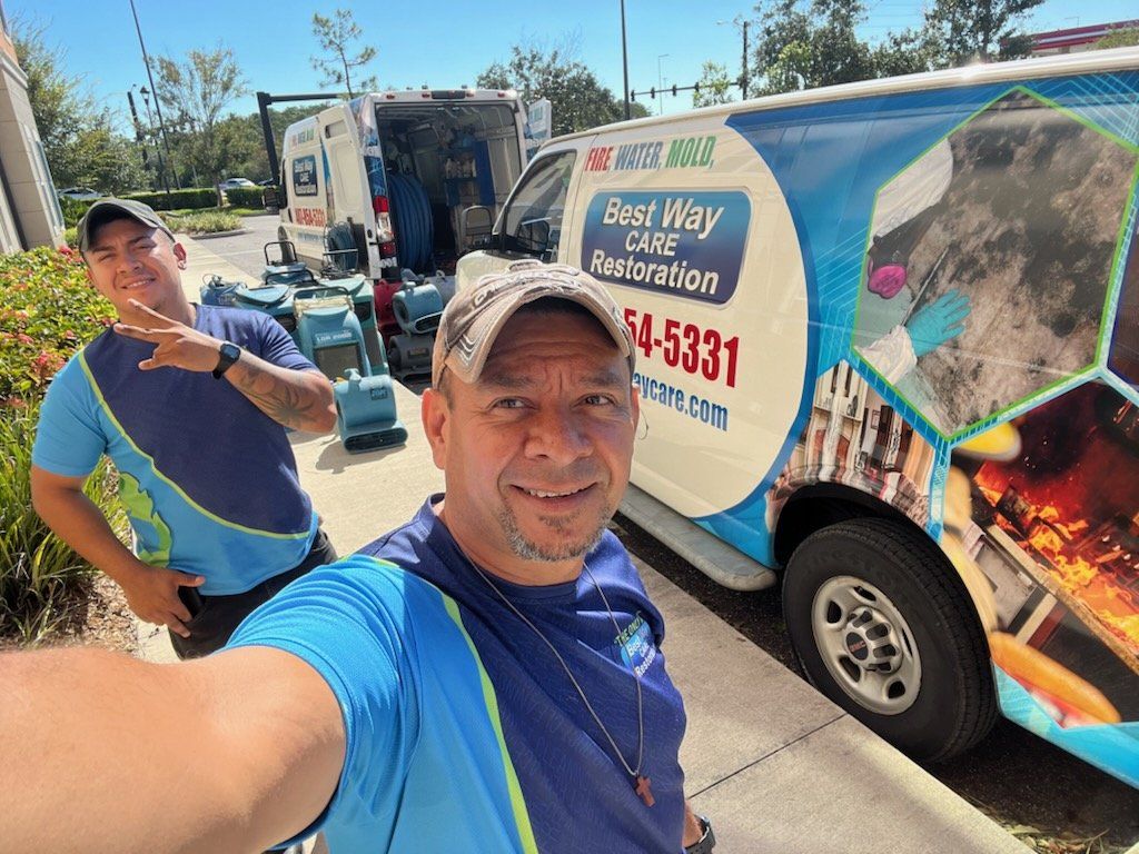 Two men pose near a branded van. One takes a selfie; the other gestures. Restoration equipment visible.