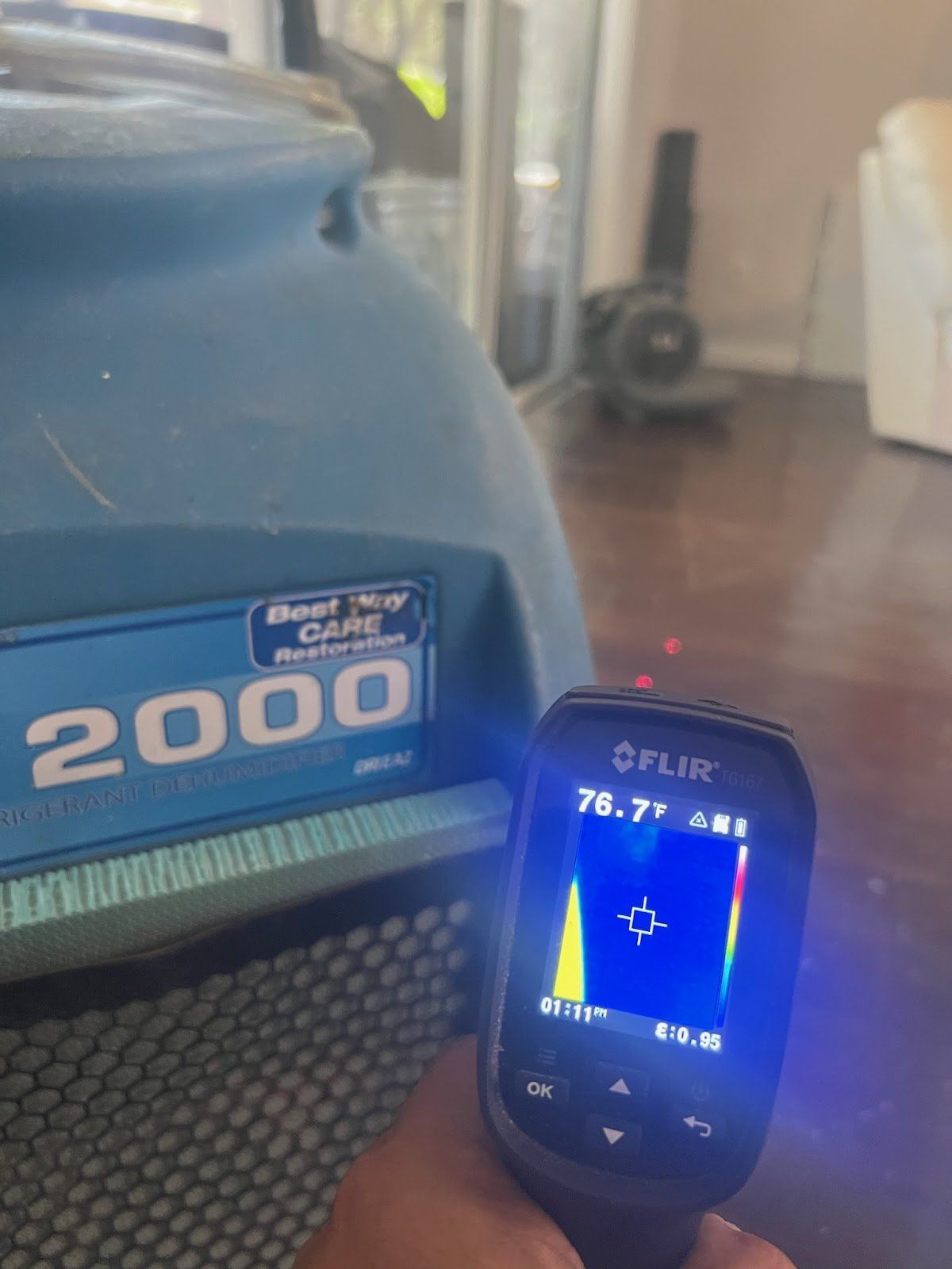 A person uses a thermal camera to measure the temperature of a blue carpet cleaner labeled 
