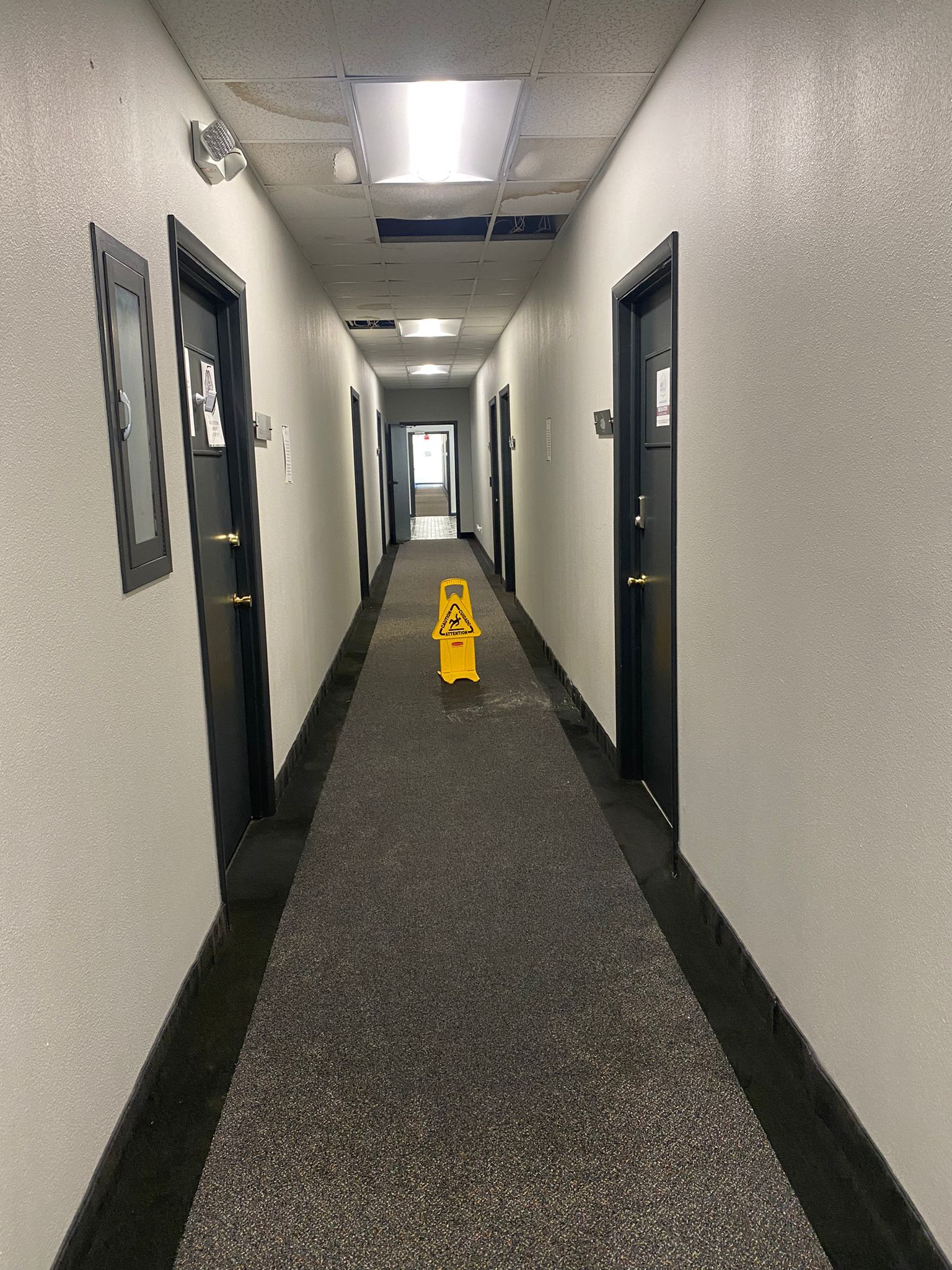 Long hallway with black doors, speckled walls, and a wet floor sign.