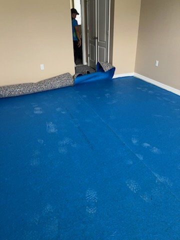 Blue floor covering installed in a room, with rolled-up carpet and a person in the doorway.