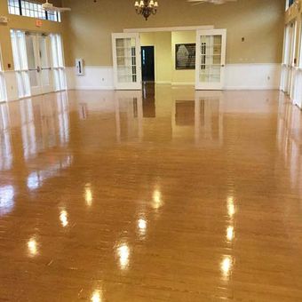 Empty, shiny hardwood floor in a large, well-lit room with white walls, doors, and curtains.