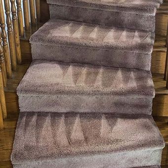 Carpeted staircase with a zig-zag pattern, light brown color, wooden banister.