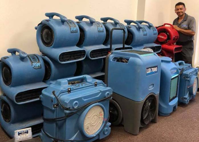 Man standing next to a collection of blue and red air movers and dehumidifiers.