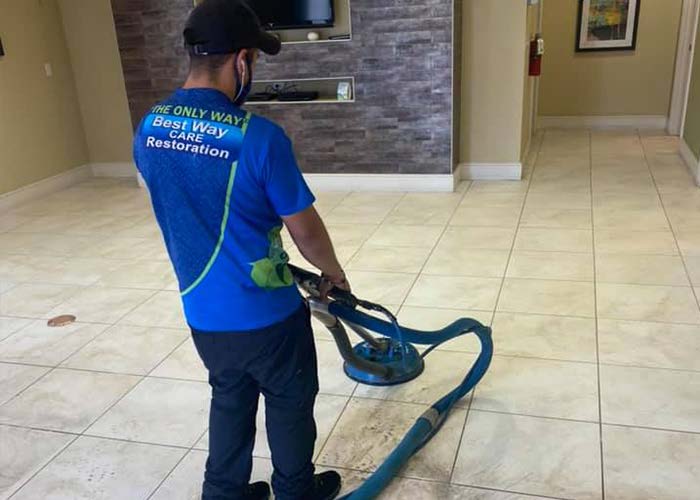 Person using floor cleaning machine in a tile-floored room.