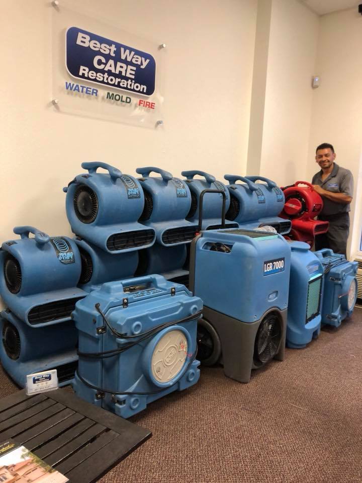 Man stands near water damage restoration equipment. Blue and red air movers and dehumidifiers in an office setting.