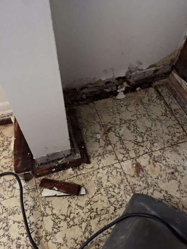 Damaged corner of a room with exposed framing, crumbling wall, and tile floor.