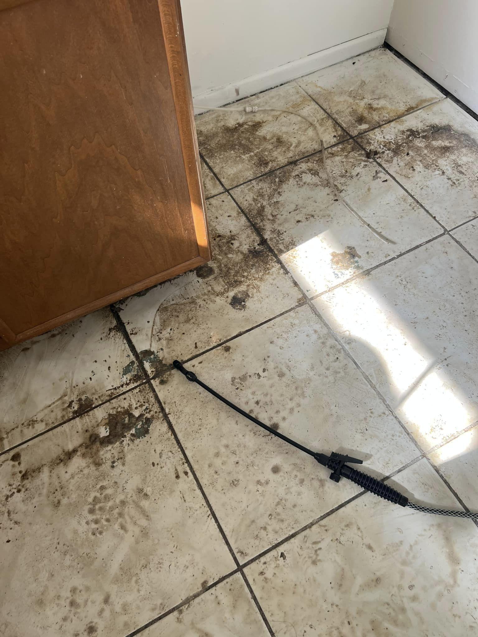 Dirty tiled floor with debris, a wooden cabinet, and a black hose.