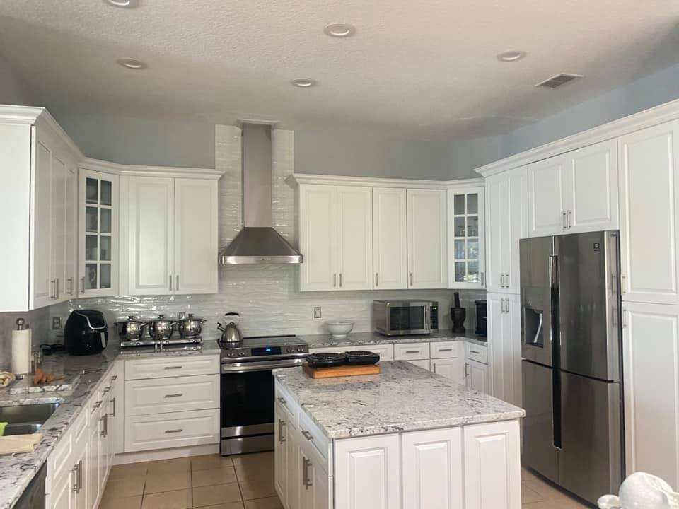 White kitchen with cabinets, stainless steel appliances, and a granite island.