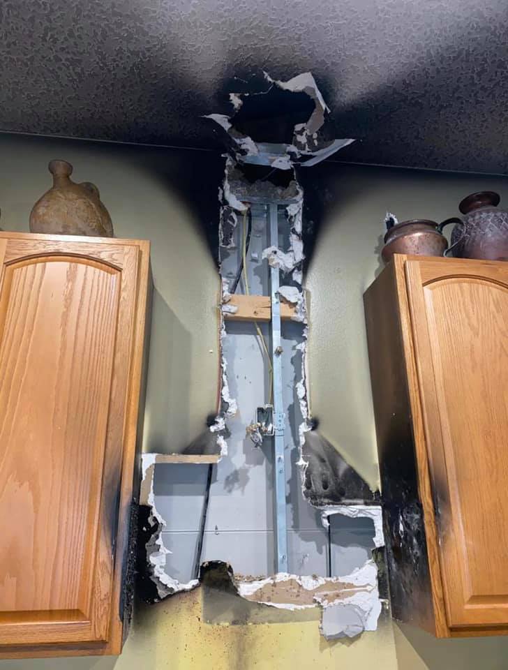 Damage from a fire, visible between kitchen cabinets. Charred ceiling and wall, exposed studs and wiring.