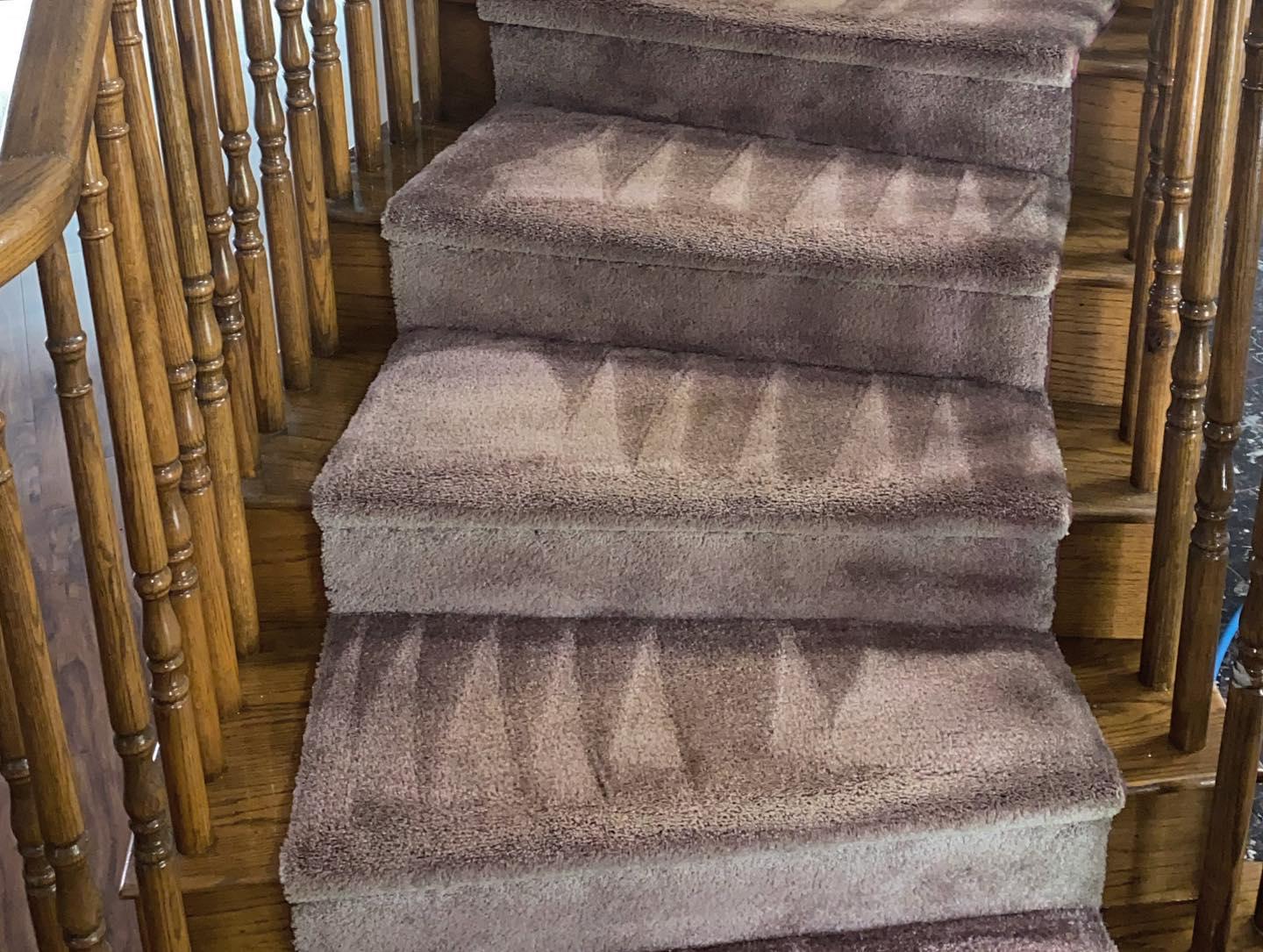 Carpeted stairs with wooden banister. The carpet is brown with a pattern.