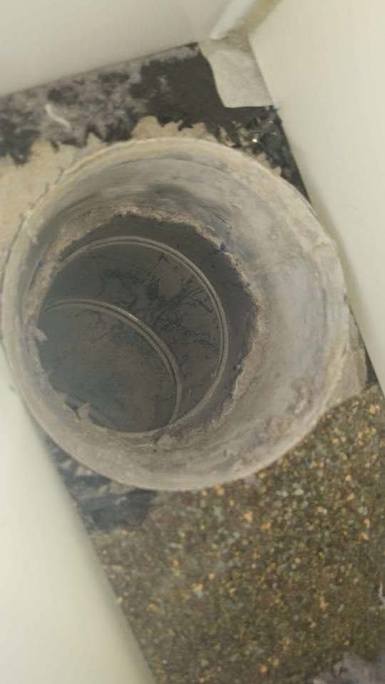 Circular air duct opening, surrounded by debris, viewed from above, indoors.