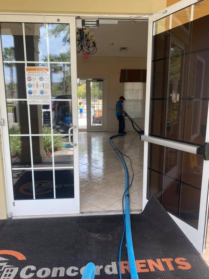 A person using a floor cleaning machine inside a building entrance.